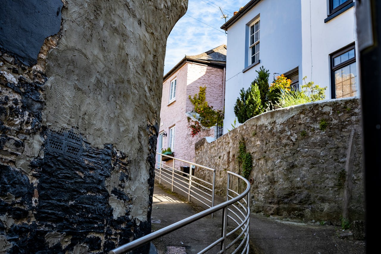 Explore the quiet charm of a narrow alley in Brixham, Devon with colorful houses and rustic walls.